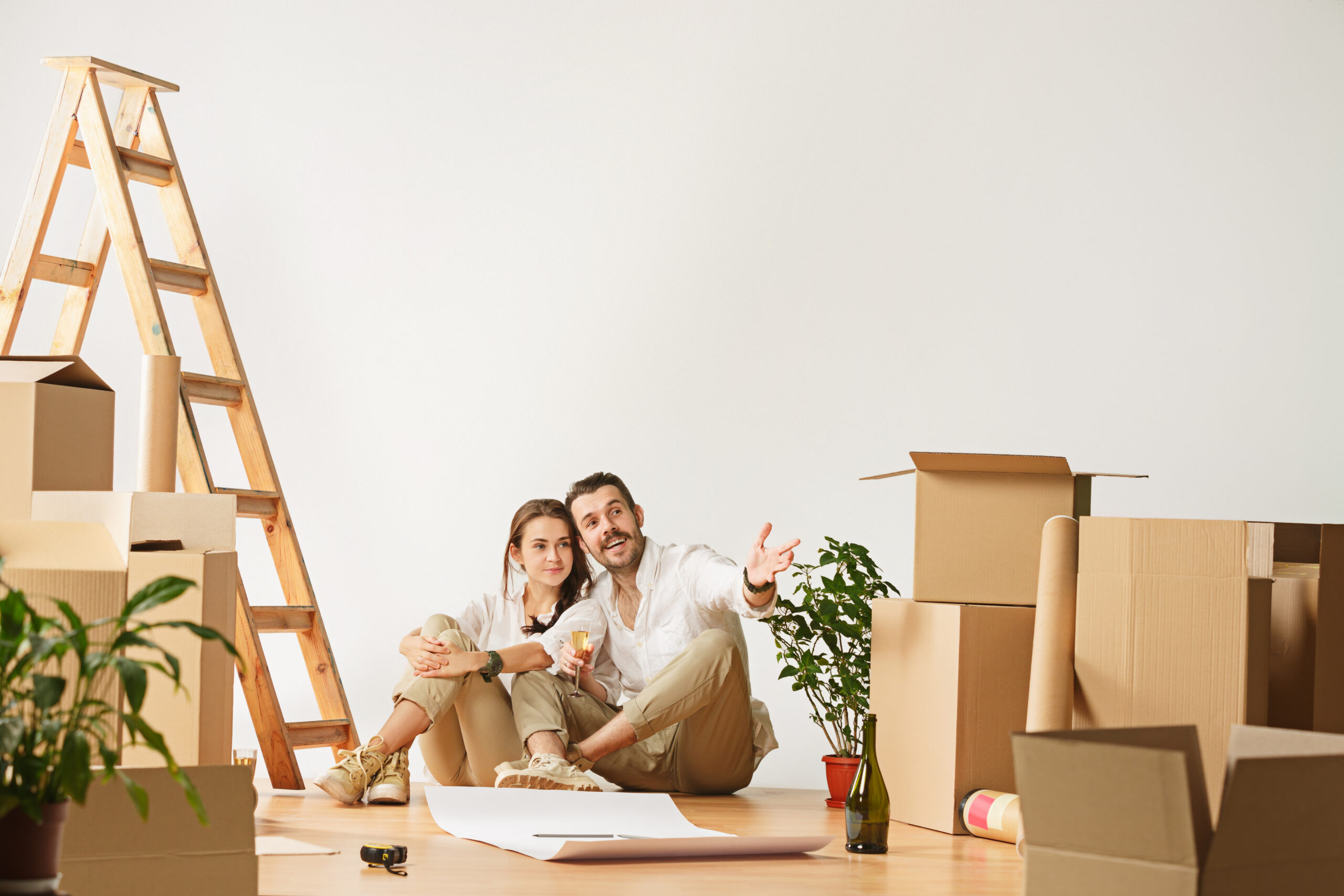 Couple souriante entourée de cartons et d’une échelle dans un intérieur en déménagement, planifiant avec des documents et plantes. comment organiser son déménagement.