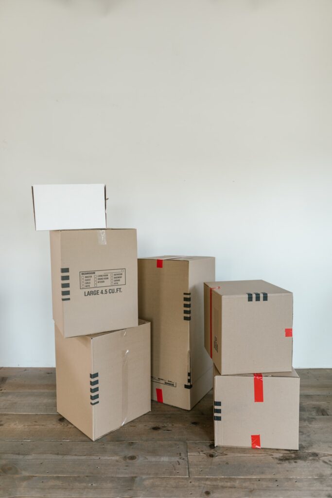 Groupe de cartons d’emballage empilés dans une pièce vide, prêts pour déménagement, sur plancher en bois. | comment organiser son déménagement