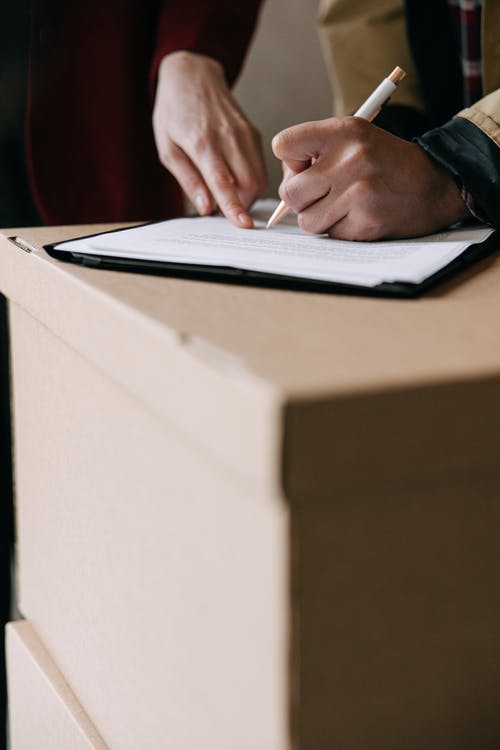Personne signant un document sur une pile de cartons, prête à planifier un déménagement. Comment bien organiser son déménagement en 1 mois.